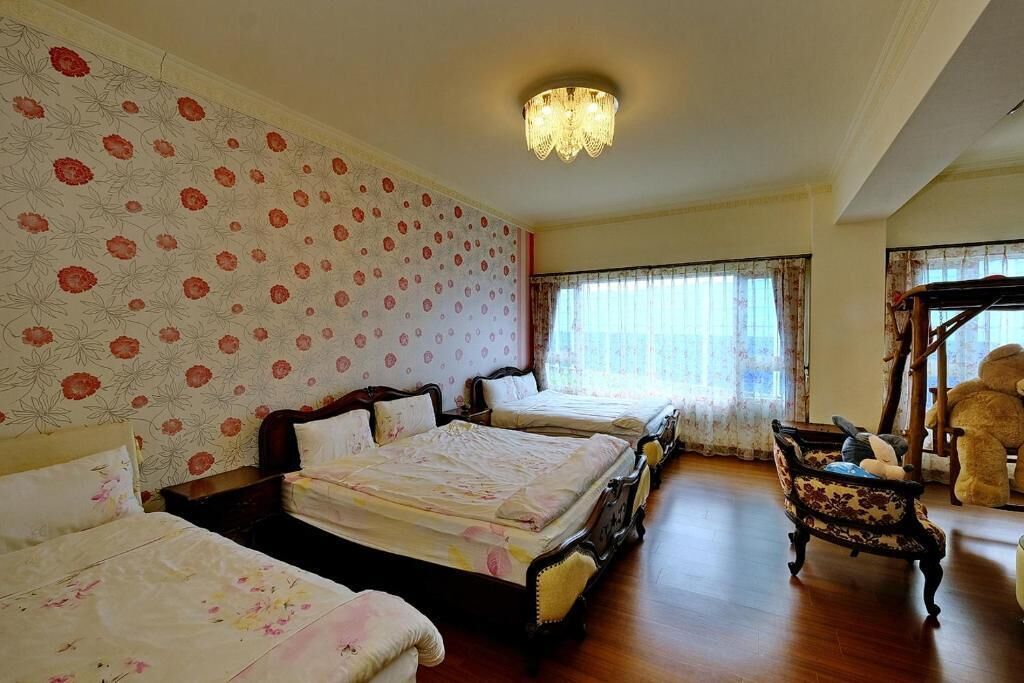 A hotel room with two beds, a chandelier, floral wallpaper, and a wooden floor.
