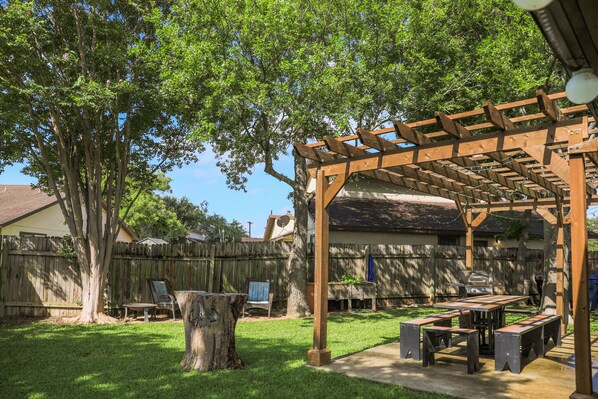 Un jardin avec une pergola en bois, un barbecue et une table de pique-nique.
