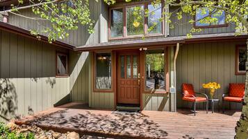 A house with a wooden deck, a front door, and two chairs with a vase of flowers.