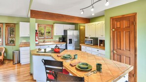 Una cocina con una isla de madera, armarios blancos, un refrigerador de acero inoxidable y un microondas.