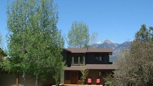 Una casa de dos pisos con un porche delantero, rodeada de árboles y una montaña al fondo.