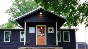 Ein niedriges Haus mit dunkler Fassade, einem Vorbau, einer Glastür und einem kleinen Seitenfenster.
