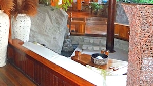 A wooden interior with a bench, decorative plants, and a view of greenery outside.