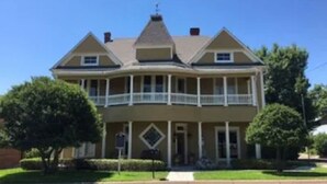 A two-story house with a balcony on the second floor, a front porch, and a chimney. - Mary Kate Doyle Suite (Granbury)