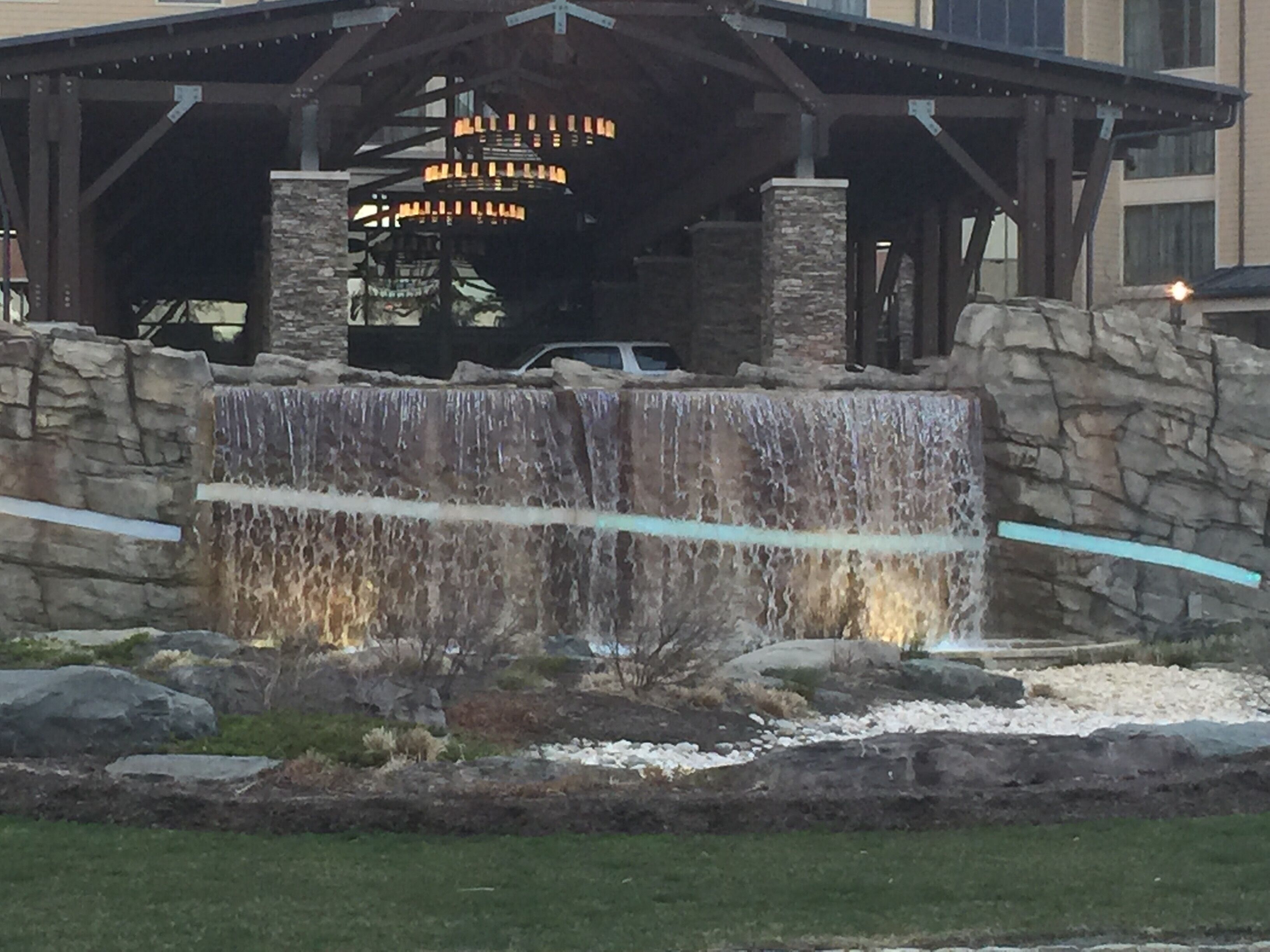 A building with a stone waterfall feature, a covered area with a chandelier, and a vehicle parked nearby.