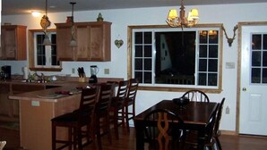 A kitchen with wooden cabinets, a dining area with a table and chairs, and a large window with a view. - Luxury, Hot Tub,Fireplace,Pool Table,Pet Friendly,No Security Deposit! (Albrightsville)