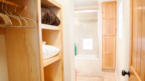 A wooden closet with shelves and hanging space, a tiled floor, and a wooden door.