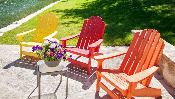 A patio with two Adirondack chairs and a small table with a flower arrangement.