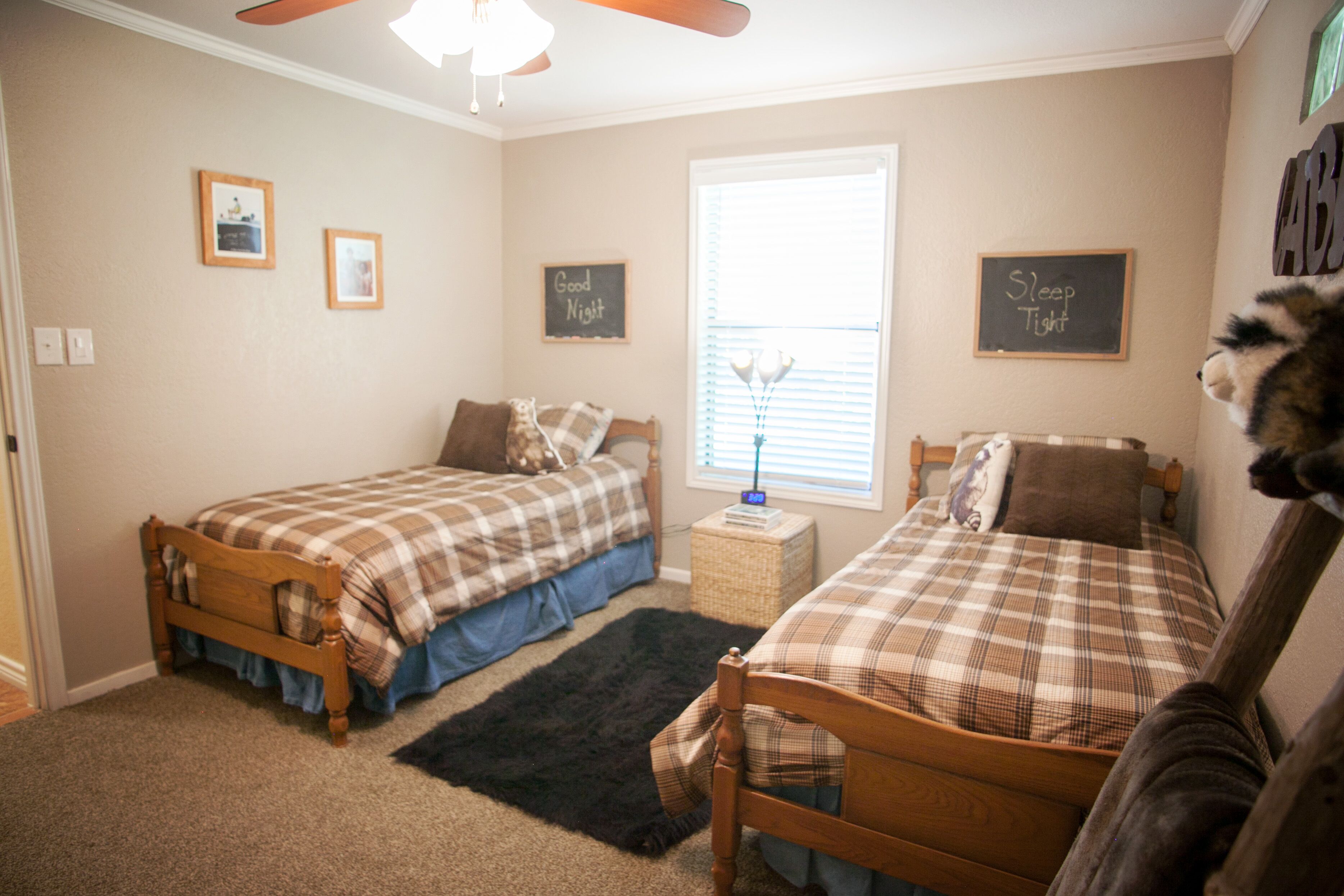 A bedroom with two beds, a window with blinds, and a ceiling fan.