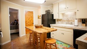 A compact kitchen with wooden countertops, a built-in refrigerator, and a small dining area with stools.