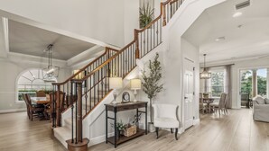 Un vaste espace de vie agrémenté d’un escalier en bois, d’une table à manger et d’un fauteuil blanc.