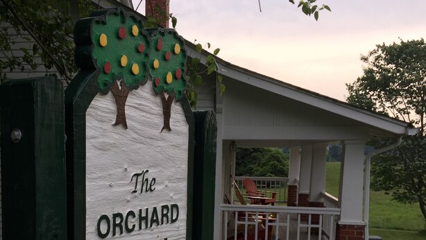 Un letrero de The Orchard Farm House con un porche y asientos al aire libre.