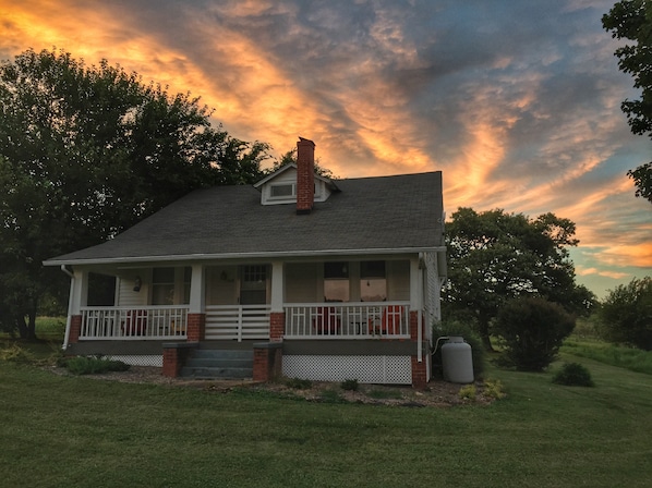A two-story house with a porch, a chimney, and a large tree in the background.
