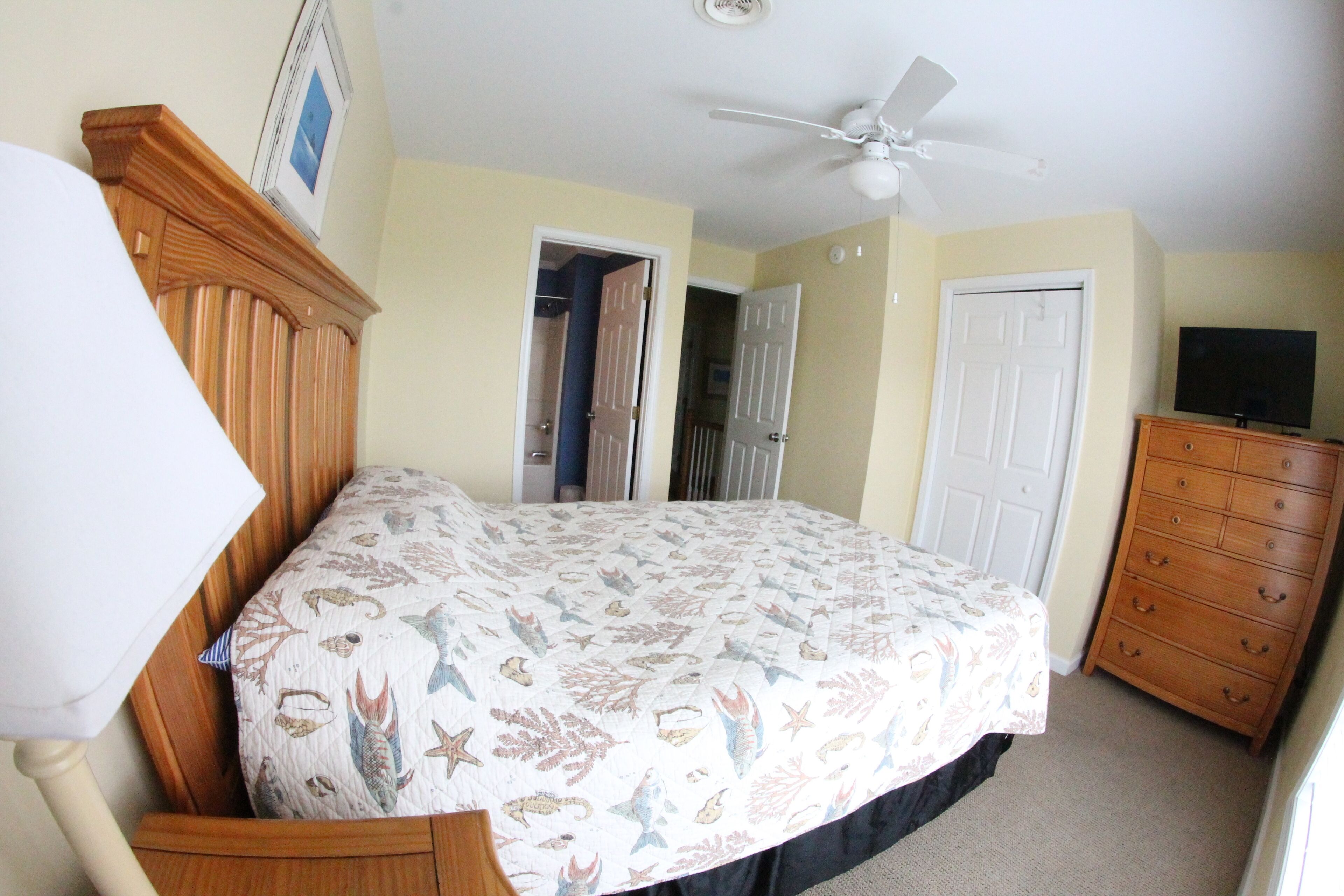 A bedroom with a bed, a dresser, a ceiling fan, and a TV.