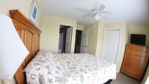 A bedroom with a bed, a dresser, a ceiling fan, and a TV.
