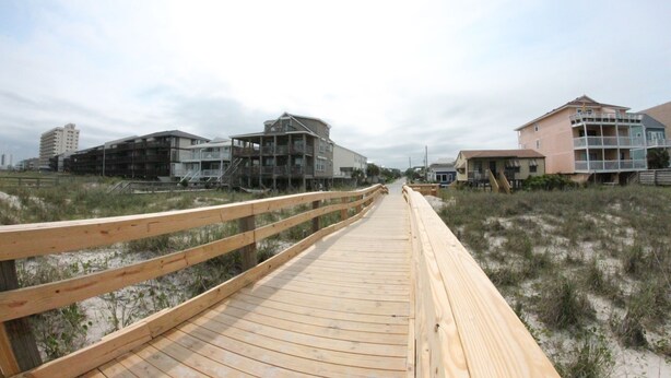 A wooden boardwalk leading to beachfront properties with multiple stories and balconies.