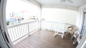 A covered porch with a ceiling fan, white railings, and two chairs.