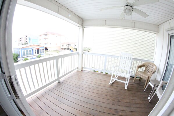 A covered porch with a ceiling fan, white railings, and two chairs.