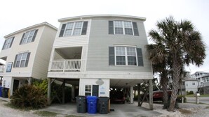 A two-story building with a balcony on the second floor, a covered parking area, and a palm tree nearby.