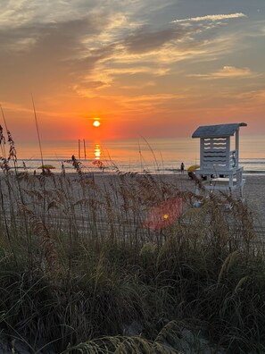 A beach scene with a lifeguard tower, ocean, and sunset.