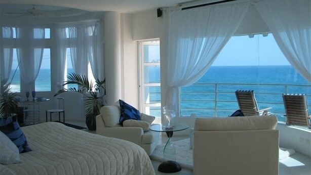 Een ruime kamer met een groot bed, een zithoek met een glazen tafel en uitzicht op de oceaan.