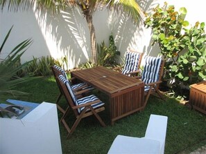 A wooden outdoor dining set with striped cushions, surrounded by lush greenery and a palm tree.