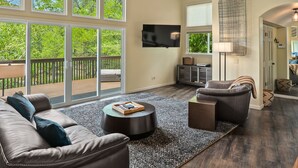 Ein geräumiges Wohnzimmer mit großem Fenster, einem Flachbildfernseher, einem Ledersofa, einem Couchtisch und einem Kamin.