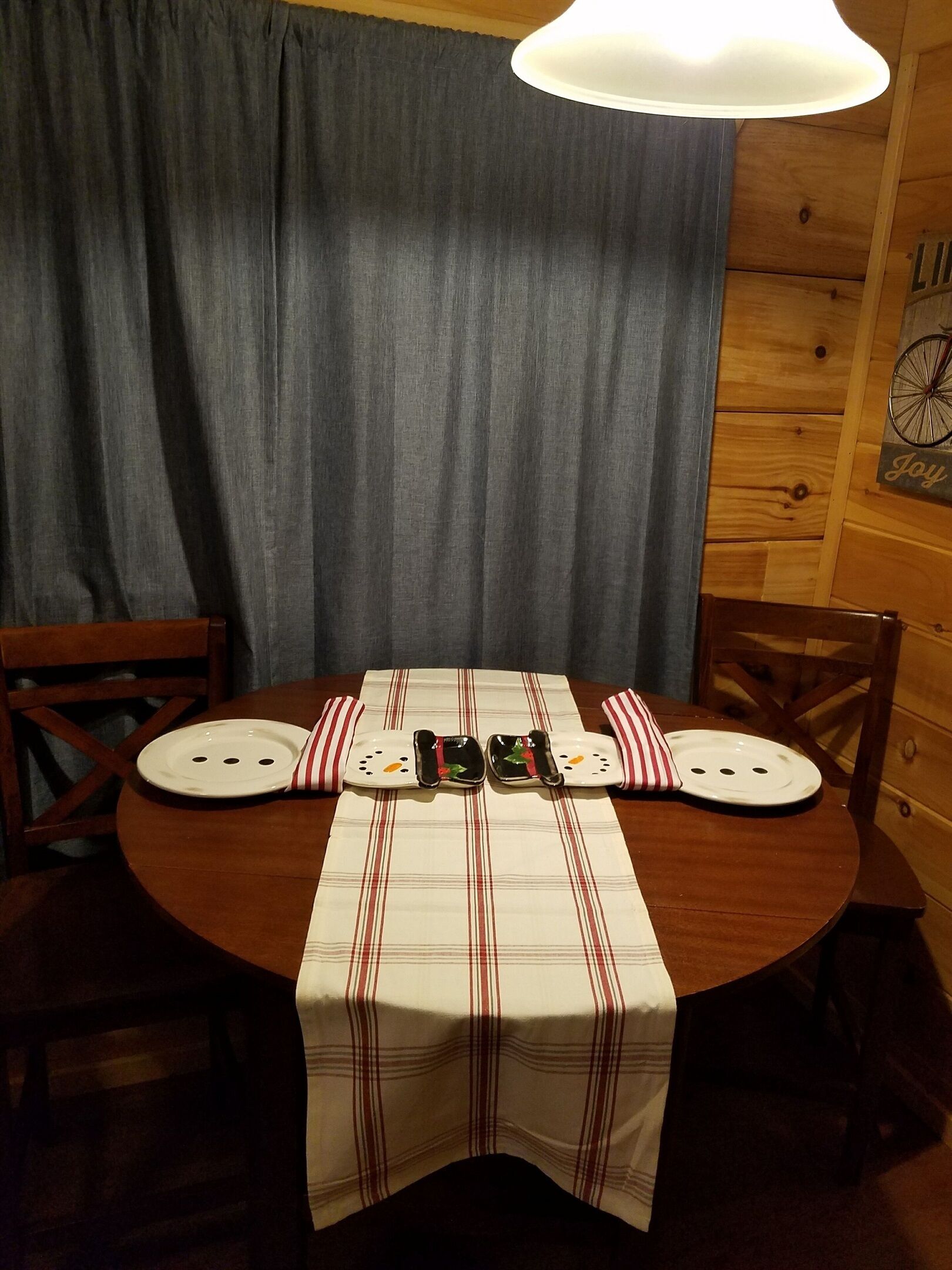Uma mesa de jantar de madeira com toalha xadrez, duas pratos brancos e um castiçal com uma vela.