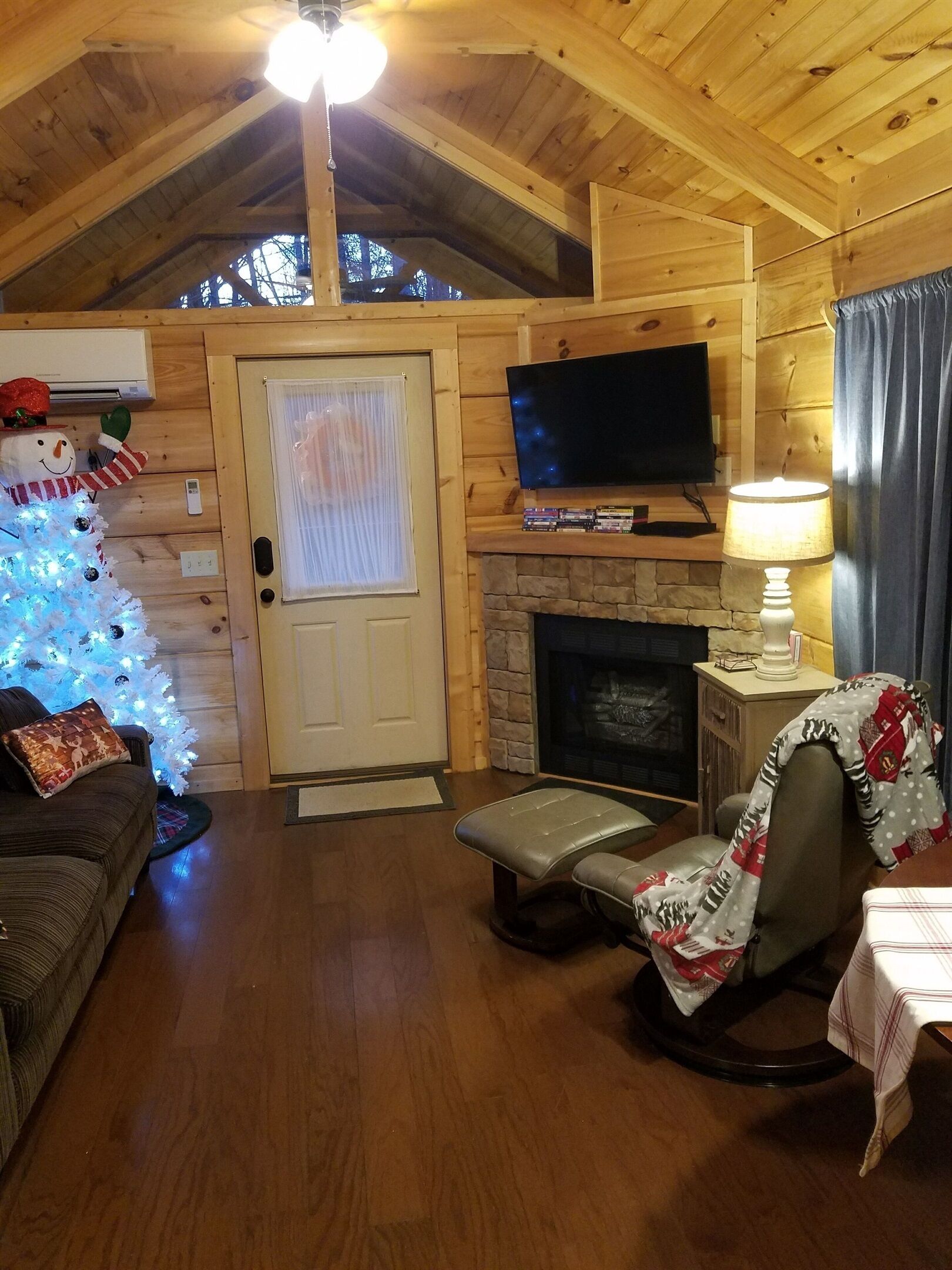 A cozy log cabin interior with a television, fireplace, and a Christmas tree.