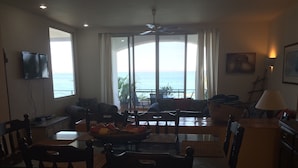 A dining area with a view of the ocean, a television mounted on the wall, and a painting on the wall. - ONLY TRUE BEACH FRONT Condo in REAL La Paz!  Full Sunset View, 2 Pools, Pool Bar (La Paz)
