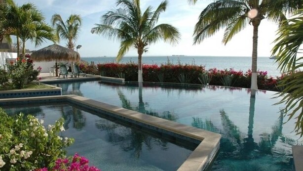 A pool area with clear water, palm trees, and a view of the ocean. - ONLY TRUE BEACH FRONT Condo in REAL La Paz!  Full Sunset View, 2 Pools, Pool Bar (La Paz)