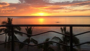 A sunset over a calm sea with palm trees in the foreground and a distant boat. - ONLY TRUE BEACH FRONT Condo in REAL La Paz!  Full Sunset View, 2 Pools, Pool Bar (La Paz)