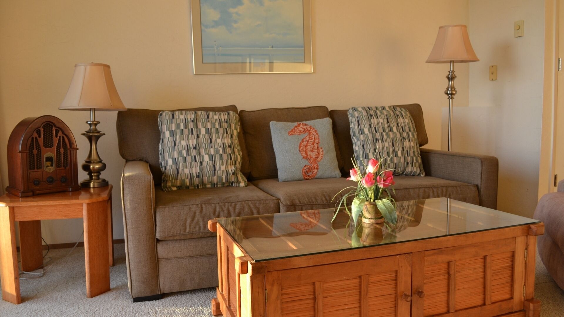 A living room with a sofa, two lamps, a radio, and a glass coffee table.
