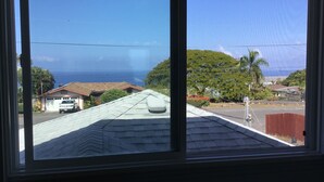 A view from a window overlooking a residential area with a clear blue sky, a white truck parked in front of a garage, and a red fence in the background. - Ocean Views In Paradise (Kailua-Kona)