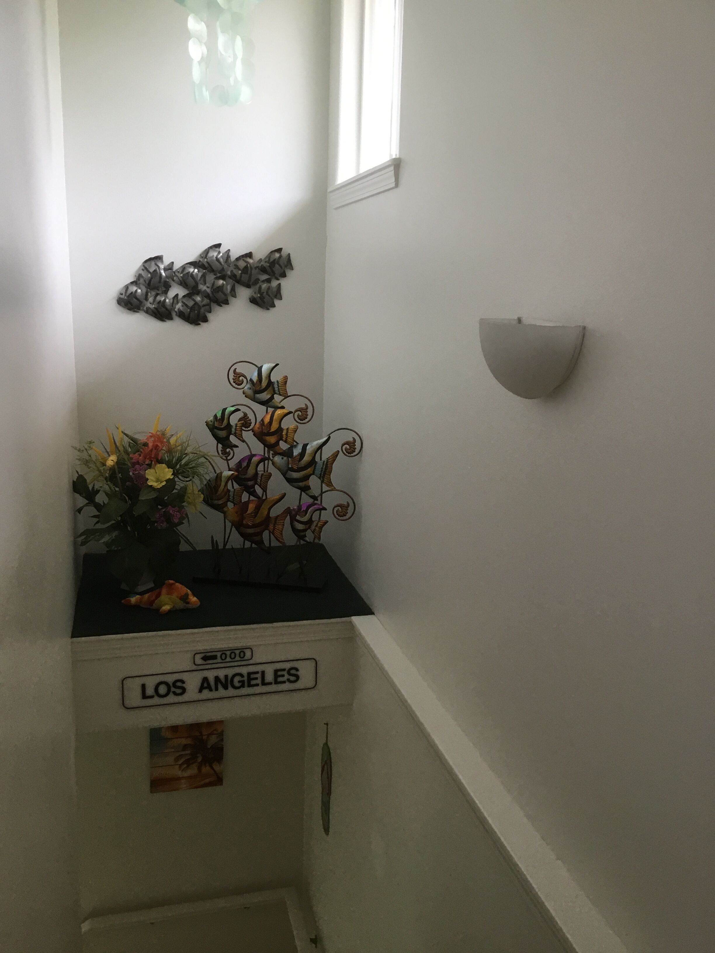 A corner of a room with a decorative wall piece, a small shelf with a vase of flowers, and a sign labeled "LOS ANGELES".