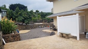 A backyard with a stone wall, a patio area, and a white pergola. - Ocean Views In Paradise (Kailua-Kona)