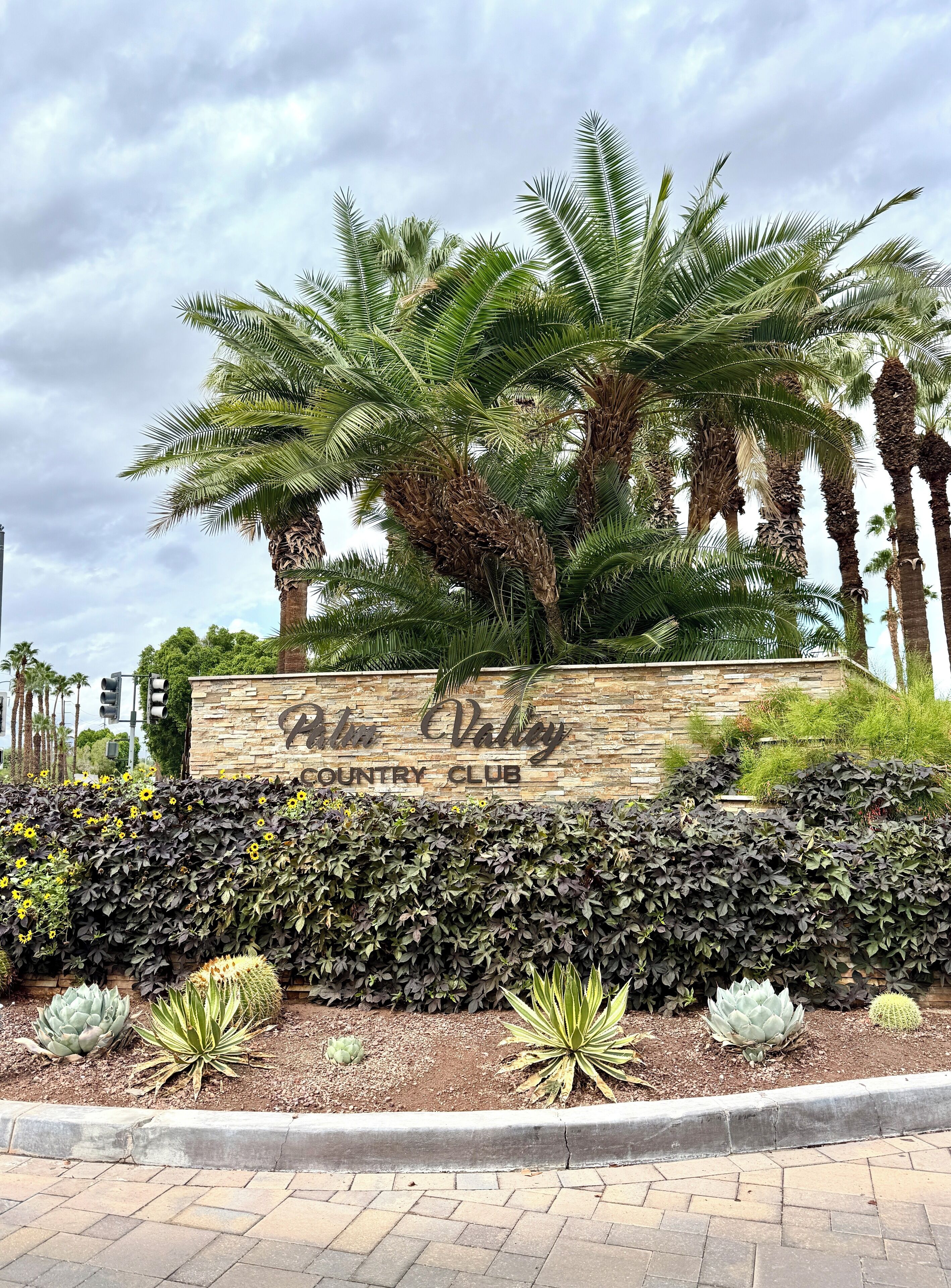 Placa do Palm Valley Country Club, rodeada por palmeiras e um jardim paisagístico com cactos e suculentas.