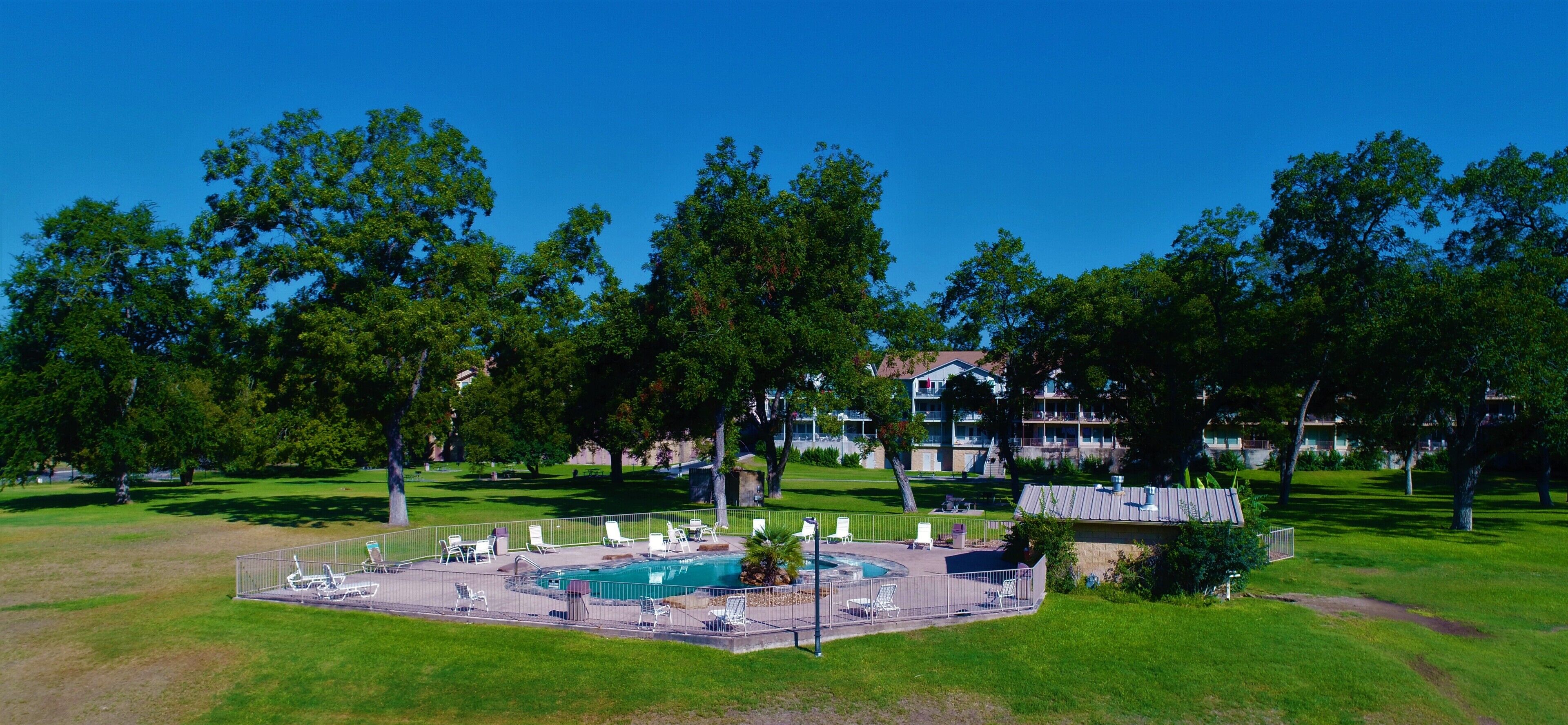 Poolbereich mit Liegestühlen und einem kleinen Pool, umgeben von Bäumen und einem Gebäude im Hintergrund.