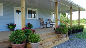 A porch with wooden chairs, potted plants, and a wooden staircase leading to the house. - Large beautiful Farmhouse in the heart of PEC - 20 minutes to Sandbanks (Prince Edward)