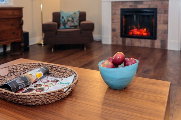 A living room with a wooden table, a blue bowl with apples, and a basket with a coffee can.