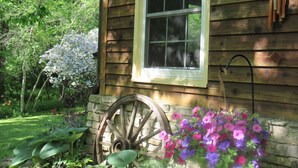 A wooden cabin with a window, a stone wall, and a wooden wheel.