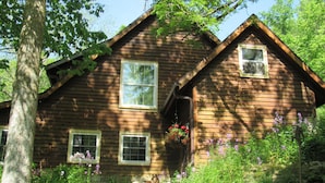A wooden cabin with two windows and a porch area with hanging flower baskets.