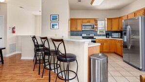 A modern kitchen with wooden cabinets, a stainless steel refrigerator, and a central island with bar stools. - Spacious Ranch Lake Retreat Hot Tub, Tesla Charger (Canyon Lake)