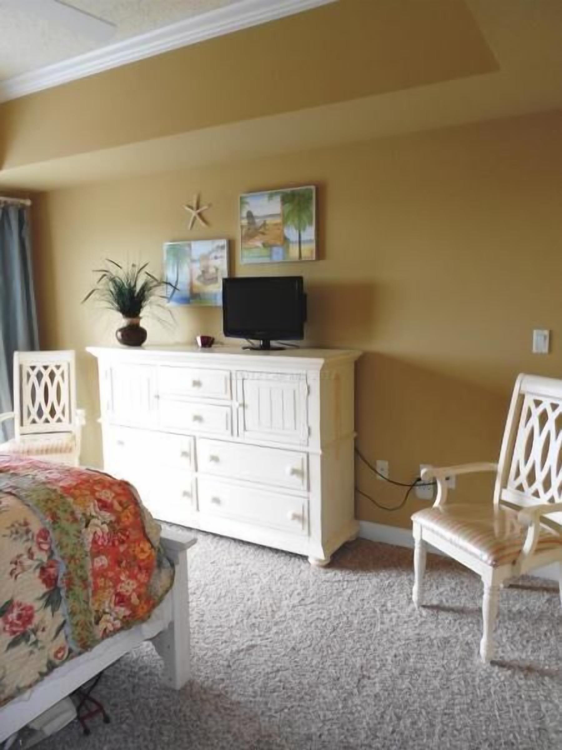 A bedroom with a bed, a dresser, a chair, and a television.