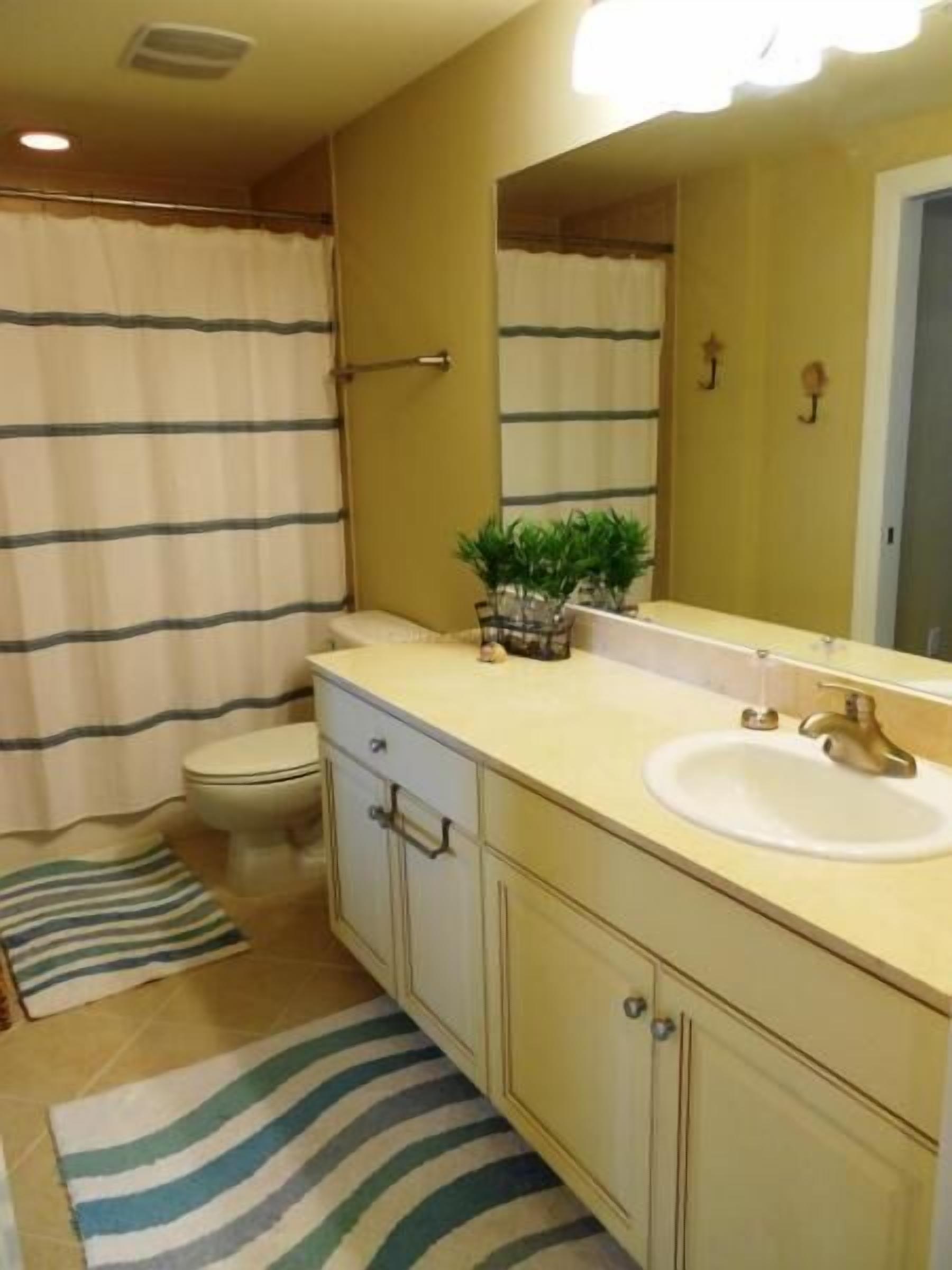 A bathroom with a toilet, sink, mirror, and striped shower curtain.