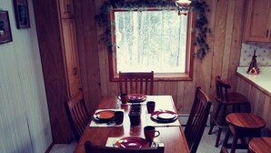 Una sala da pranzo in legno con un tavolo imbandito per quattro persone, sedie, una finestra vista alberi e un angolo cottura con un fornello.