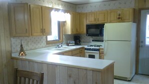 Una cucina con mobili in legno, un piano di lavoro bianco, un fornello, un forno a microonde e un frigorifero.