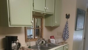 Een keuken met groene kastjes, een koffiezetapparaat, een spoelbak en een vloerkleed.