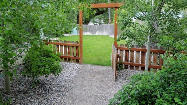 Een houten pergola met een grindpad dat naar een houten poort leidt.