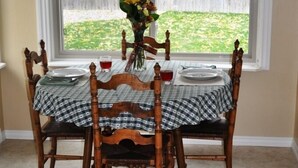 Een eettafel met een geruit tafelkleed, vier houten stoelen en een vaas met bloemen.